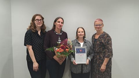 Lastenkirjainstituutin neljän työntekijää. Yhdellä on kädessään kukkakimppu, toisella diplomi. 