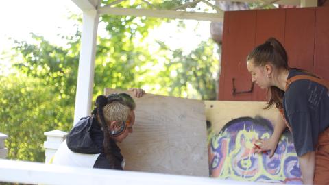 Two people are carrying sheets of plywood for an art project.