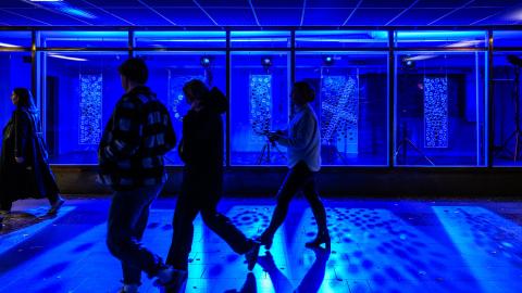 People walking at the 2024 Window Walkabout event in front of a blue light art installation.