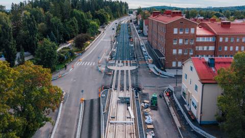 Kuvassa keskellä raitiotietyömaa ja autokaistoja, vihreää vasemmalla ja punatiilinen koulu oikealla. 