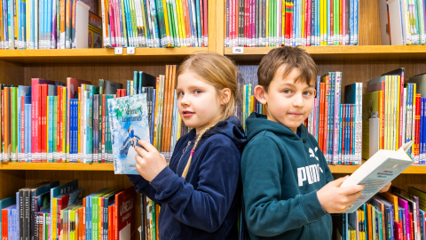 Two people reading books in front of a bookcase.