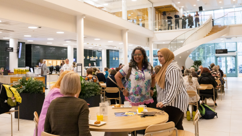 There are lots of people sitting at tables having a coffee in a large, bright hall. 