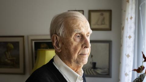 A person looks out of a window, with paintings visible in the background.