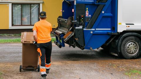 Kuvassa tyhjennysauto ja kuljettaja siirtämässä jäteastiaa. 