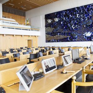 Tyhjä kaupunginvaltuuston istuntosali pöytine ja tuoleineen.