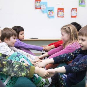 Children sitting hand in hand, facing each other on the floor.