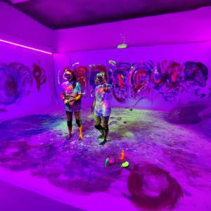 Violettisävyisessä kuvassa kaksi henkilöä virtuaalilasit päässä huoneessa, jossa taidetta seinillä.