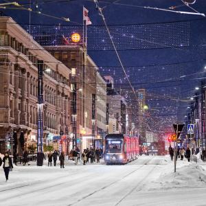Lumisateessa ihmisiä ja raitiovaunu Hämeenkadulla illalla.