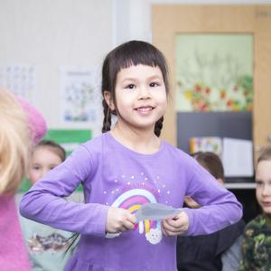 Children in a classroom, a girl with dark hair looks at the camera.