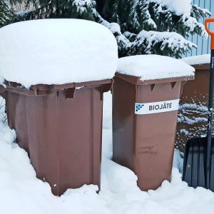 Pihalla lumisia jäteastioita ja lumilapio.