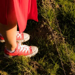 Henkilöstä, jolla on päällään punainen hame ja kengät ja joka seisoo nurmikolla, näkyy vain jalat.