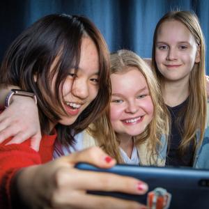 Kolme nuorta ottamassa selfietä sinistä taustaa vasten.