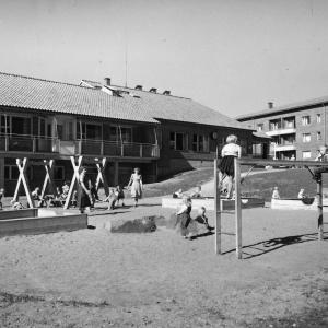 Mustavalkoisessa kuvassa Kalevan lastentalon pihamaan leikkialuetta, jossa muun muassa hiekkalaatikko ja kiipeilyteline.