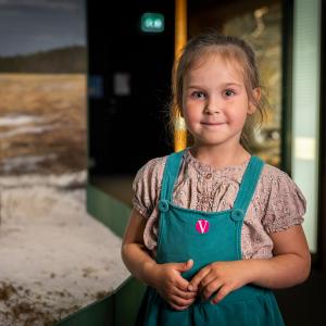 Pieni tyttö hymyilee kameralle, taustalla museon näyttelyä.