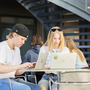 Lukion opiskelijat istuvat pöydän ääressä ja tekevät töitä tietokoneilla.