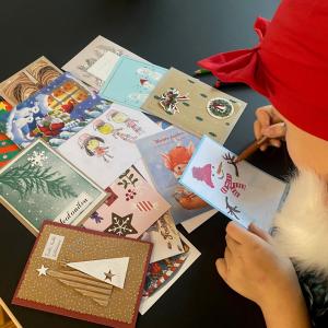 Lapsi tonttulakissa piirtämässä joulukorttia. Pöydällä kortteja.