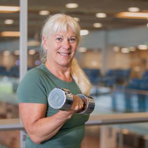 Hymyilevä vanhempi nainen kuntoilee kuntosalilla.