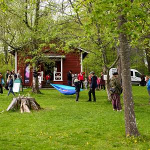 Ihmisiä vihreässä puistossa, jossa on värikkäitä taideteoksia. Osa ripustaa riippumattoja. 