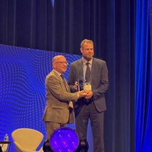 Mies ojentaa palkintoa toiselle miehelle palkintogaalan lavalla.