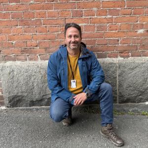 Klaus smiles directly at the camera while kneeling.