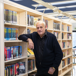 Henkilö nojaa kyynärpäällään yhteen kirjaston monista kirjahyllyistä.