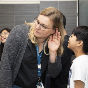 Lapsi kuiskaa opettajan korvaan. Taustalla toinen lapsi.