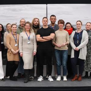 Kolmetoista henkilöä seisoo pienellä korokkeella. Taustalla ilmakuvaa Tampereen keskustasta.