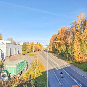 Autotie, pyörä- ja jalankulkuväylät ja kulkijoita syysväreissä olevien puiden ympäröimän, vasemmalla rakennus.
