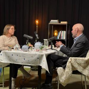 Nainen ja mies keskustelevat teepöydän ympärillä podcast-lavasteissa. 