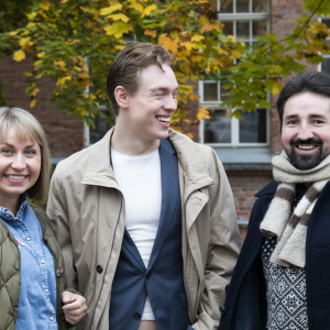 Three people are standing in front of a colourful tree in autumn.