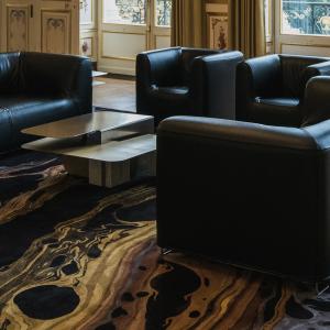 Huoneessa lattialla tumma matto, jossa on vaaleita kuvioita. Huoneessa keskellä on tumma sohvaryhmä ja nojatuolit.