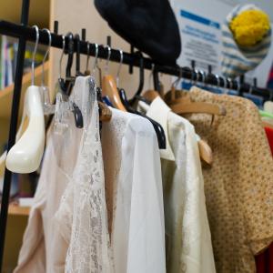 Vaaterekki, jossa roikkuu paitoja. Rekin päällä on pipoja. Takana on hylly.