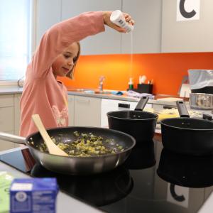 Kouluikäinen tyttö maustaa ruokaa kasvisruokakurssilla.