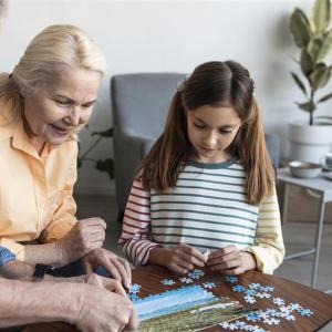 Isoäiti ja isoiso istuvat sohvapöydän ääressä kokoamassa palapeliä tummahiuksisen lapsen kanssa.