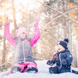 Kuvassa kaksi lasta istuu lumihangessa ja heittää lunta.