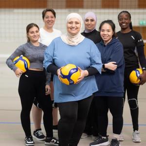 Kuusi naista lentopallokentällä ryhmäkuvassa. Kolmella heistä on lentopallo kädessään. 