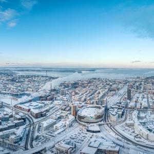 Ilmakuvassa levittäytyy luminen Tampere. Keskellä Nokia Arena ja risteilevät tiet, taustalla järvet ja sininen taivas.