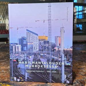 Kirjan kansikuvassa urbaani Tampereen keskusta. Kirja on kuvattu puulattialla, taustalla museon metallikaidetta.