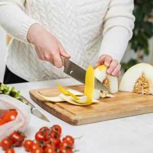 Ruonlaittaja leikkaa hunajamelonia. Pöydällä on myös tomaatteja ja salaattia.