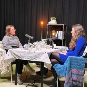 Aino-Maija Vaskelainen ja Anna-Kaisa Ikonen istuvat vastakkain pöydän äärellä podcast-studiossa. 