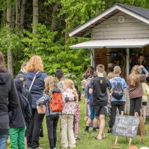 Ihmisiä jonottamassa puiseen koppiin, josta kaksi nuorta jakaa ruokaa.