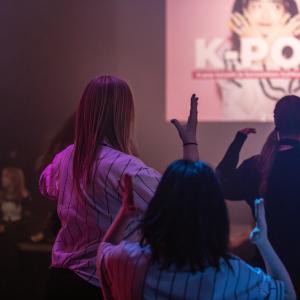 Ryhmä nuoria tanssii salissa, jonka seinällä on heijastettu kuva, jonka päällä lukee k-pop
