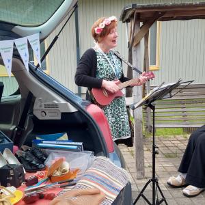 Nainen soittaa ukulelea kukkaseppele päässään ja laulaa yleisölle.