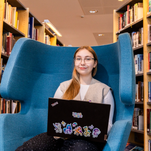 Opiskelija Daria Panova istuu nojatuolissa tietokone edessään ja takana näkyy kirjahyllyjä.