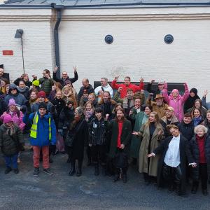 Noin 60 ihmistä ryhmäkuvassa vanhan rakennuksen edustalla. 