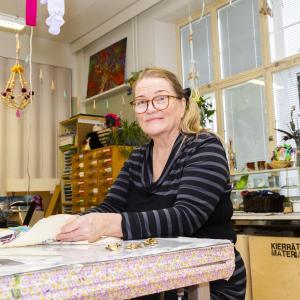 Raitapaitainen nainen tekee käsityötä Monitoimitalon kädentaitopajassa.