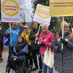 Hymyileviä ihmisiä mielenosoituskylttejä käsissään. Niissä lukee Kaikkien Tampere ja Tampereen kaupungin vanhusneuvosto.