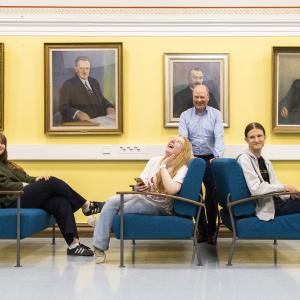 Miia Kaldenbach, Venla Vuorinen ja Sasu Länsiö istuvat tuoleilla opettaja Tomi Anttilasta heidän takanaan luokkakäytävällä.
