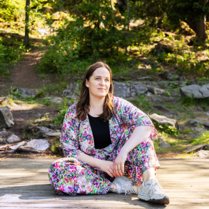 A person is sitting at the beginning of the pier, with rocks and a forest behind them.