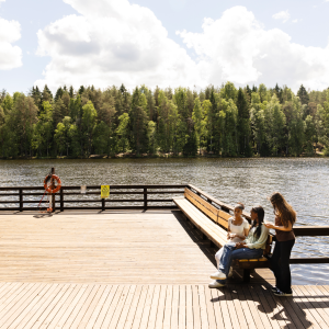 Yksi mies kalastamassa ja kolme nuorta tyttöä istumassa Ahvenisjärven uudistetulla laiturilla poutaisena kesäpäivänä. 